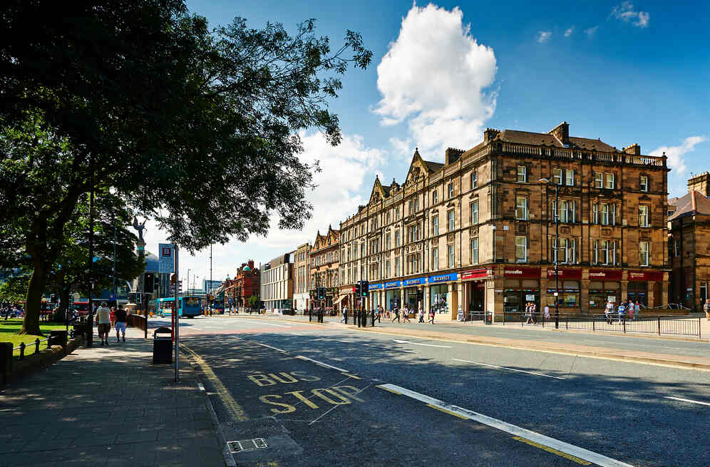 A stone building in a city, with a coffee shop and other establishments on the ground level.